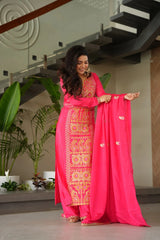 Woman in a bright pink traditional outfit with gold patterns indoors.
