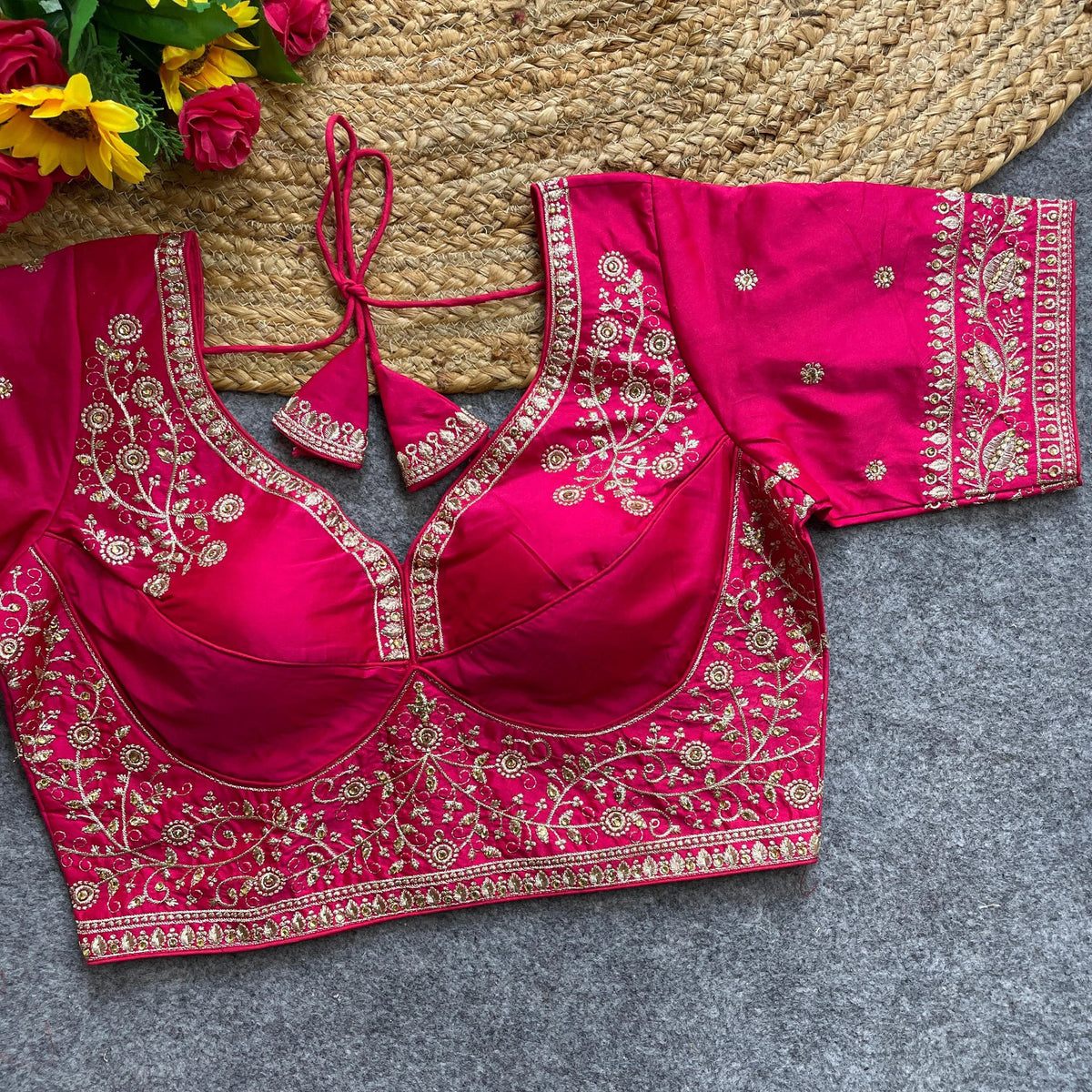 Pink embroidered blouse on a textured surface with flowers in the background