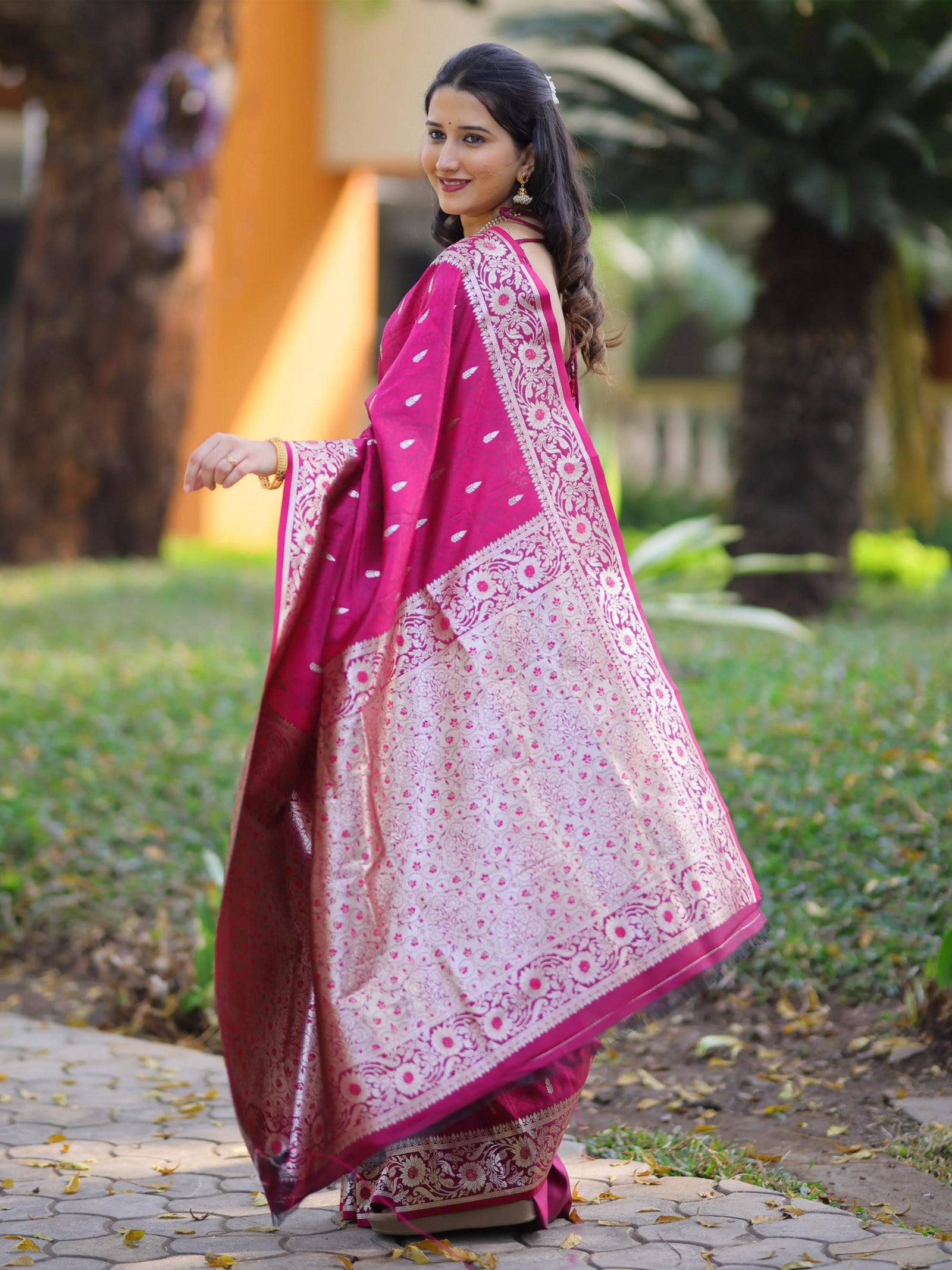Woman wearing a traditional saree with a pink and white pattern in an outdoor setting.