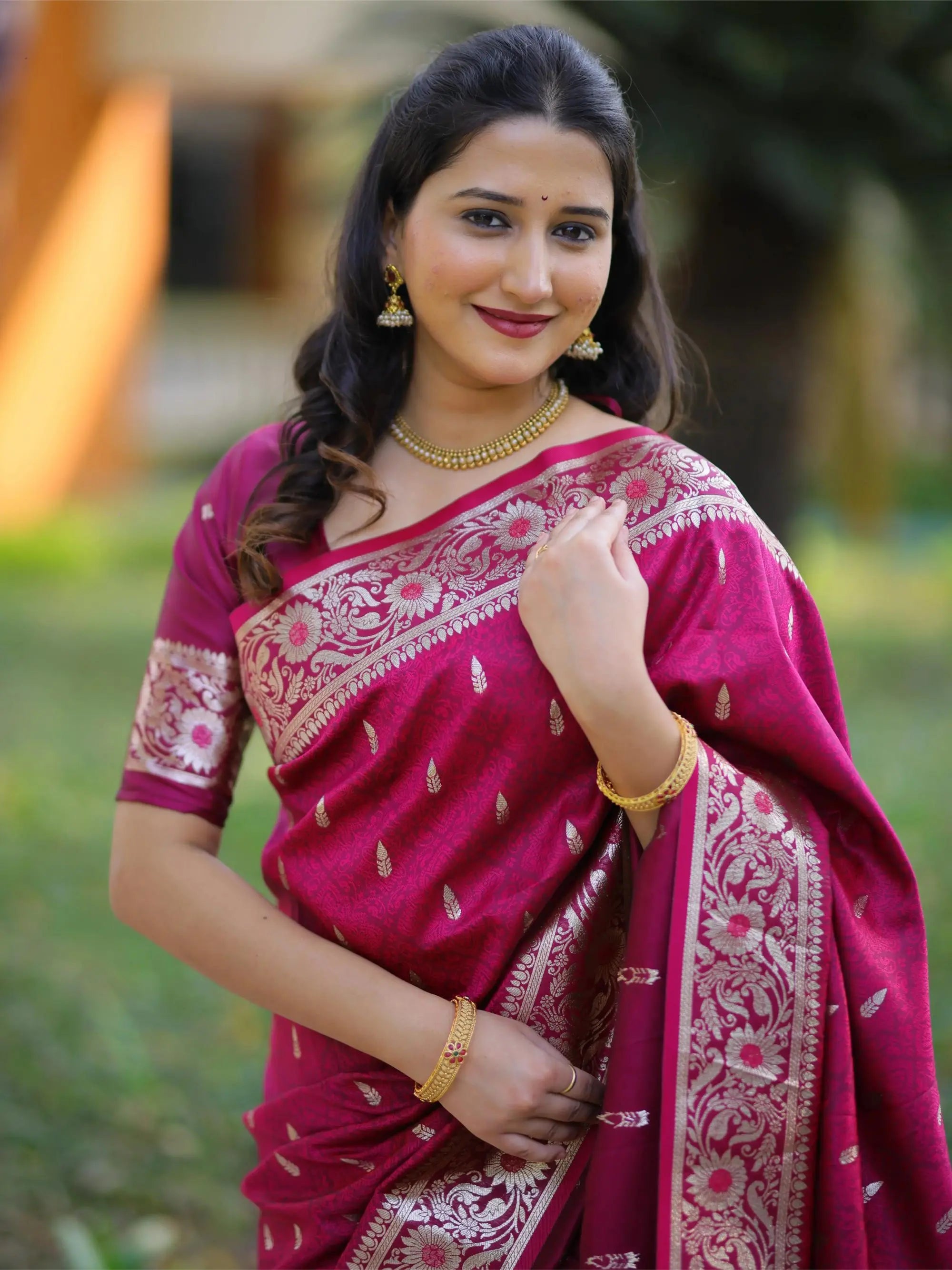 Woman wearing a pink saree with white patterns against a blurred natural background