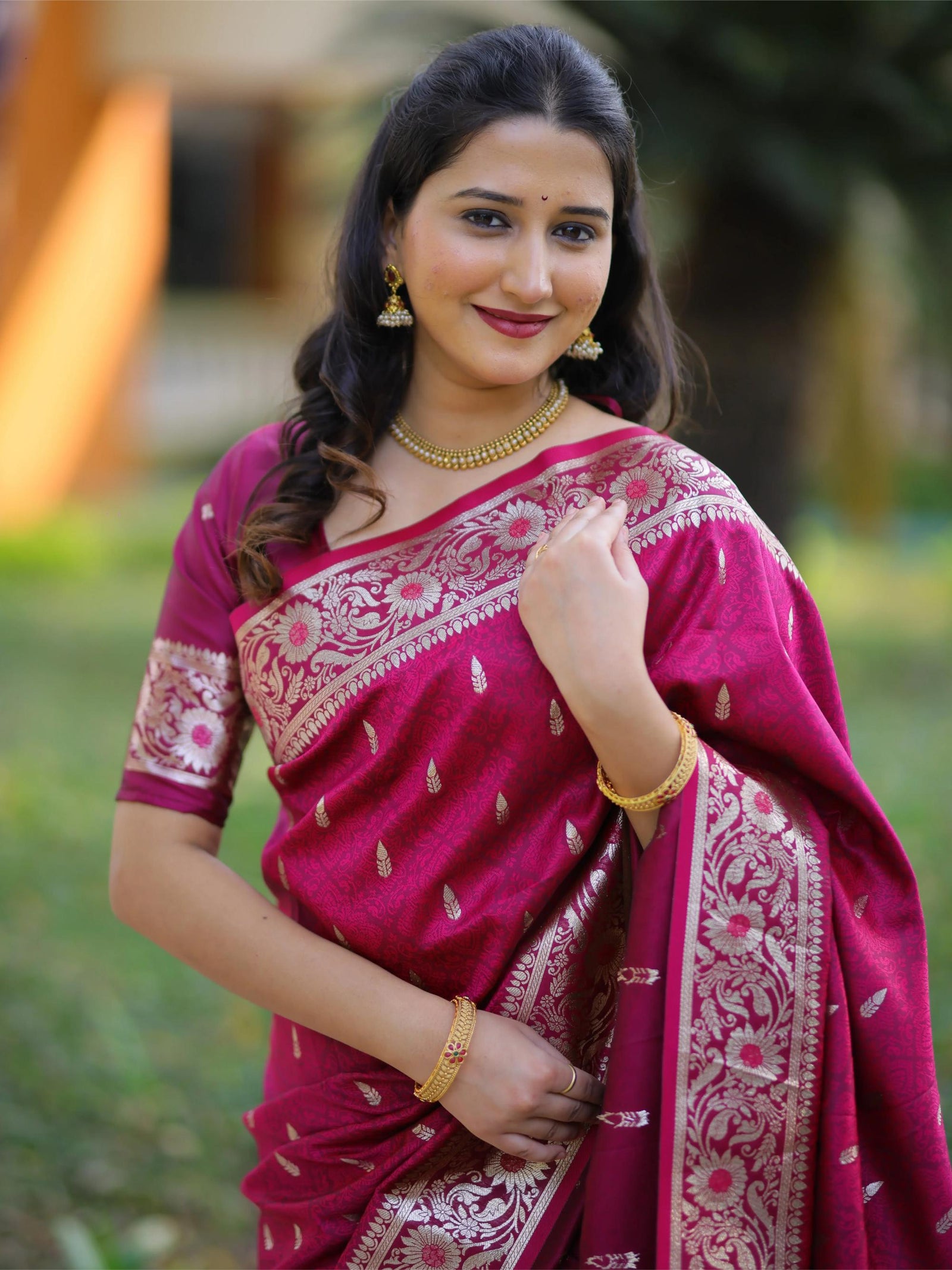 Woman wearing a pink saree with white patterns against a blurred natural background
