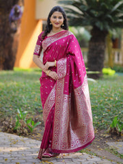 Woman wearing a pink saree with a pattern, standing outdoors on a path with greenery.