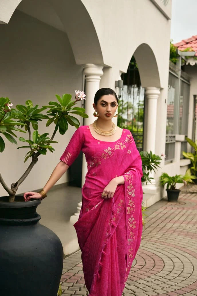 Woman in a pink saree standing in front of a building with arches and plants.