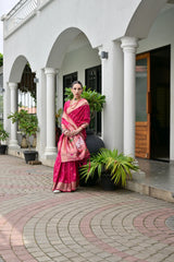 Woman in a pink saree standing in front of a white building with columns.