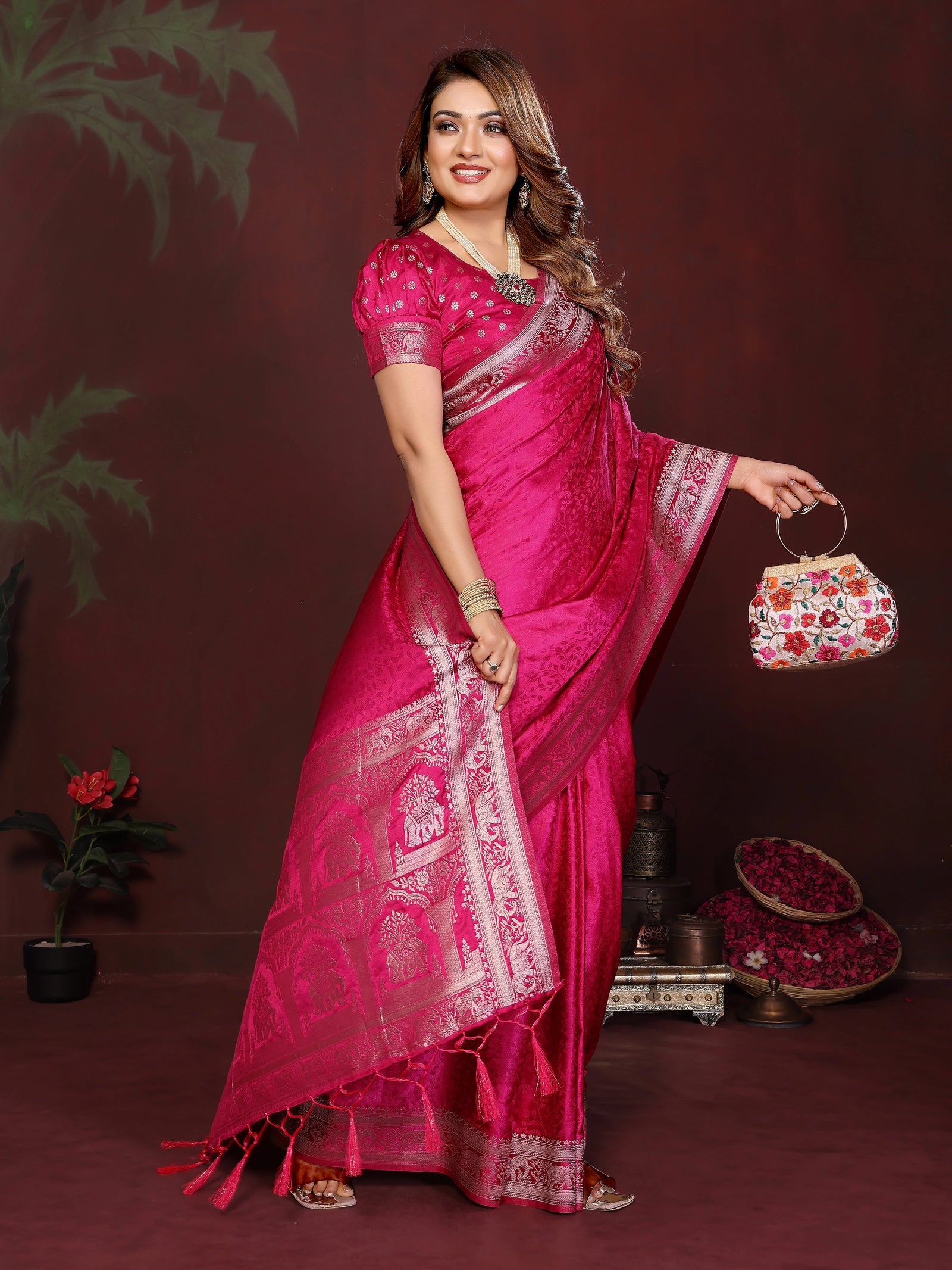 Woman in a pink saree holding a decorative bag against a dark background