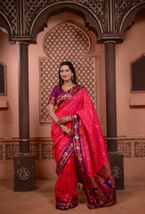 Woman in a vibrant pink saree with intricate patterns standing in an ornate architectural setting.