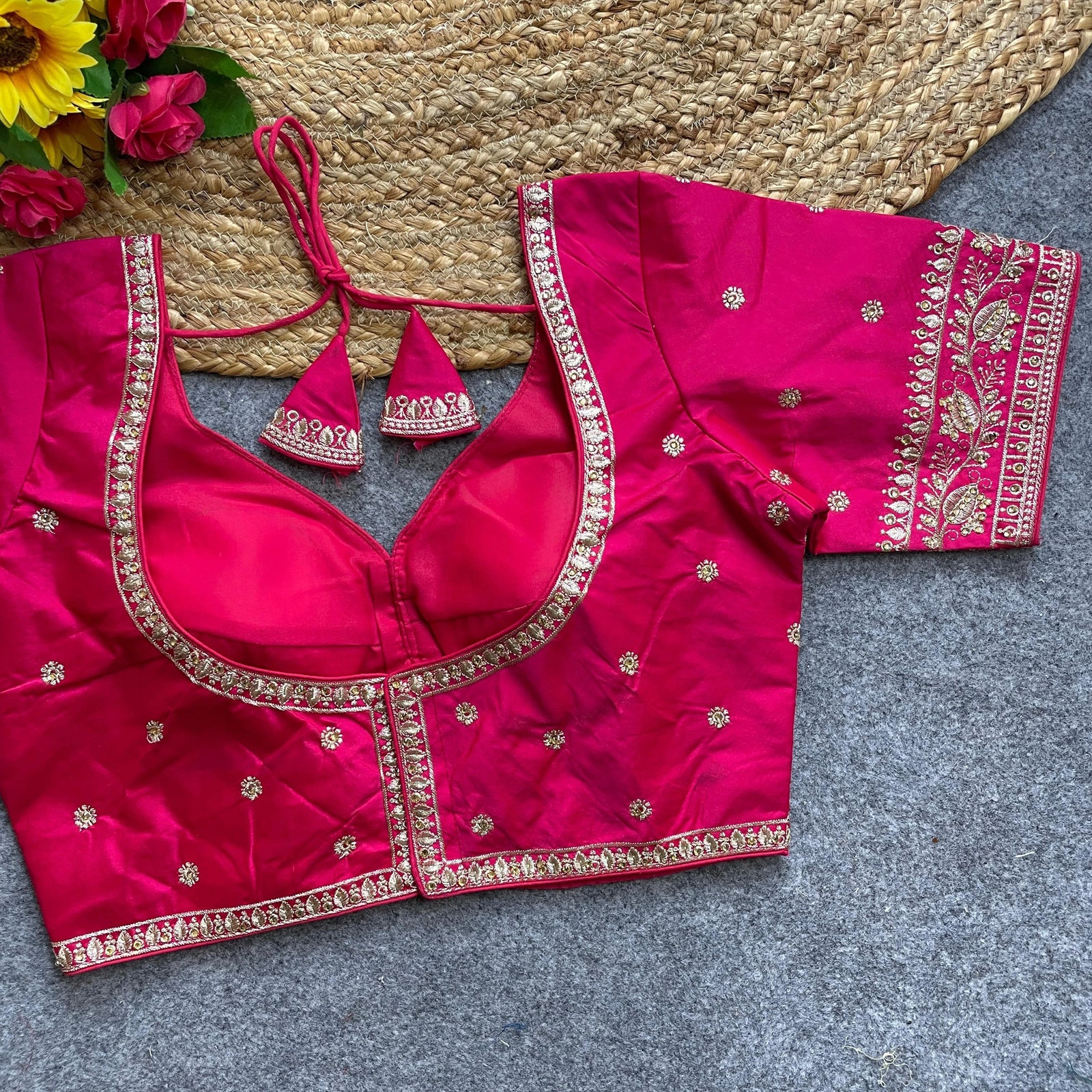 Pink embroidered blouse with gold detailing on a textured surface with flowers.