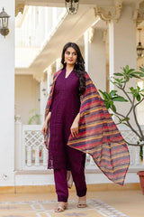 Woman in a purple traditional outfit with a colorful shawl standing in a decorative indoor setting.
