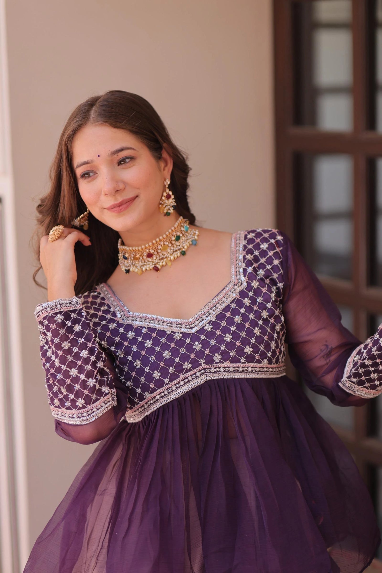 Woman wearing a purple traditional outfit with gold jewelry indoors.
