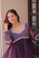 Woman wearing a purple traditional outfit with gold jewelry indoors.