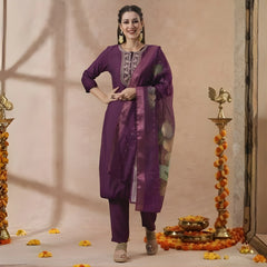 Woman in a purple traditional outfit standing in front of decorative elements on a beige background