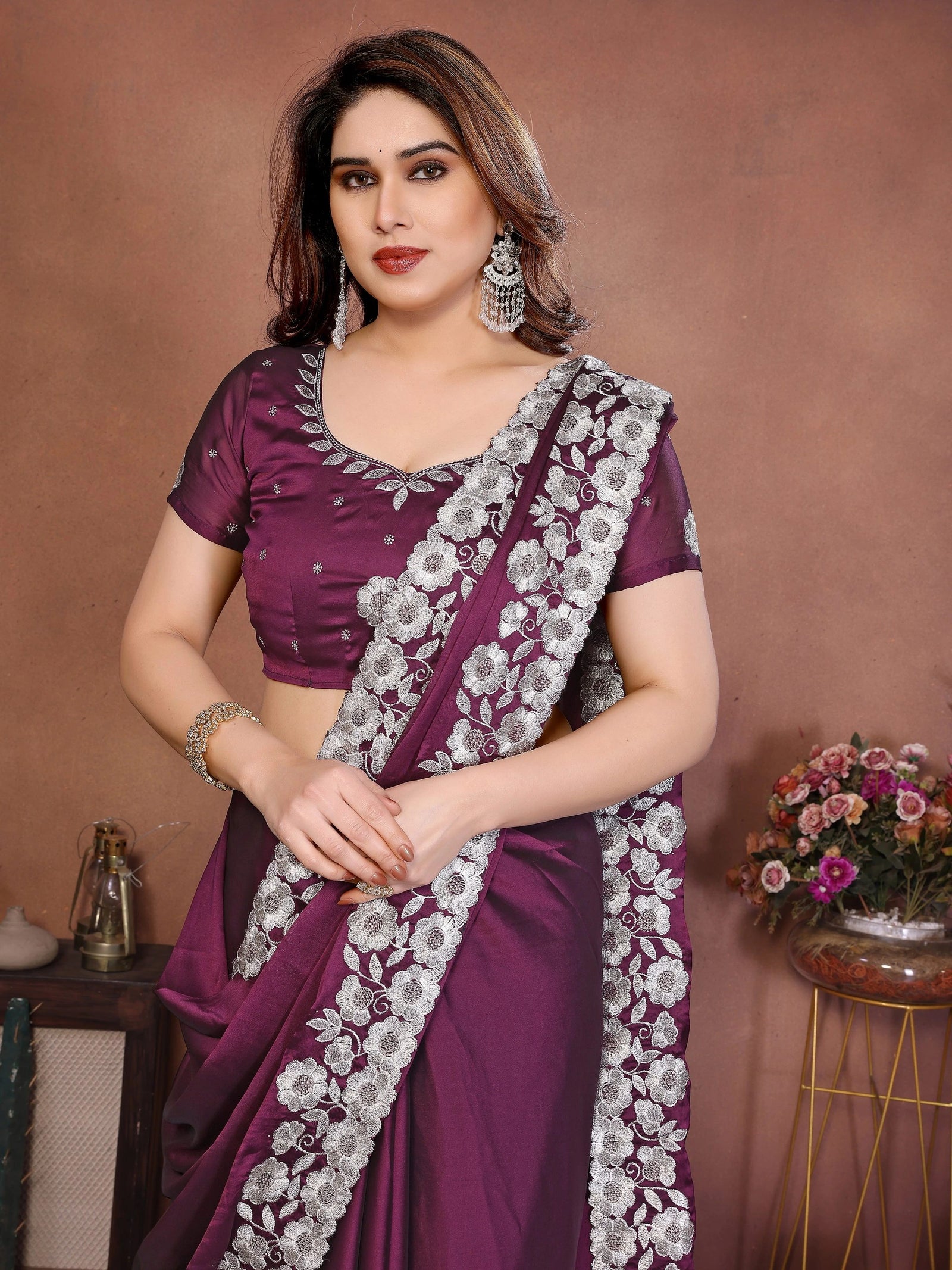 Woman wearing a purple saree with white floral patterns against a brown background