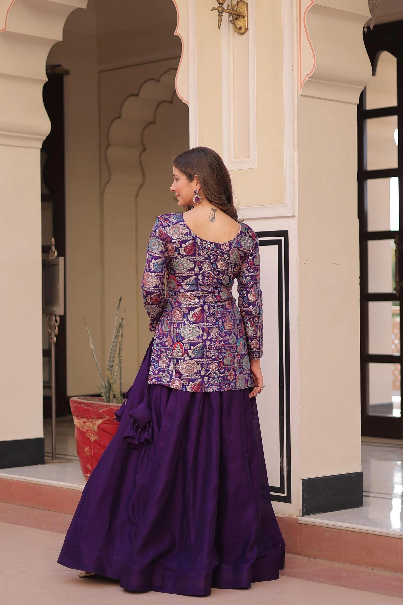 Woman in a traditional purple outfit standing in an ornate indoor setting.