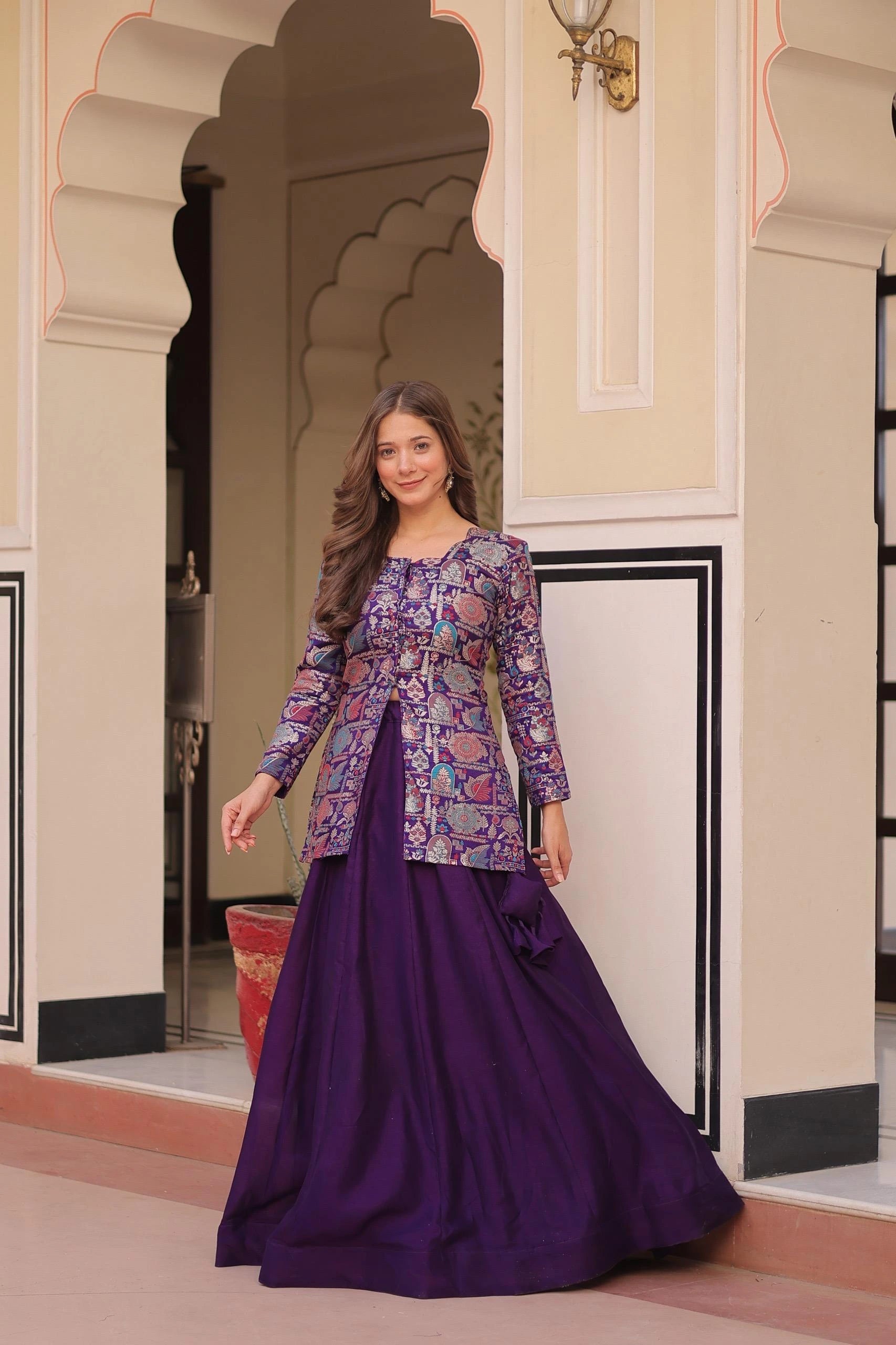 Woman in a patterned top and purple skirt standing in an ornate doorway.