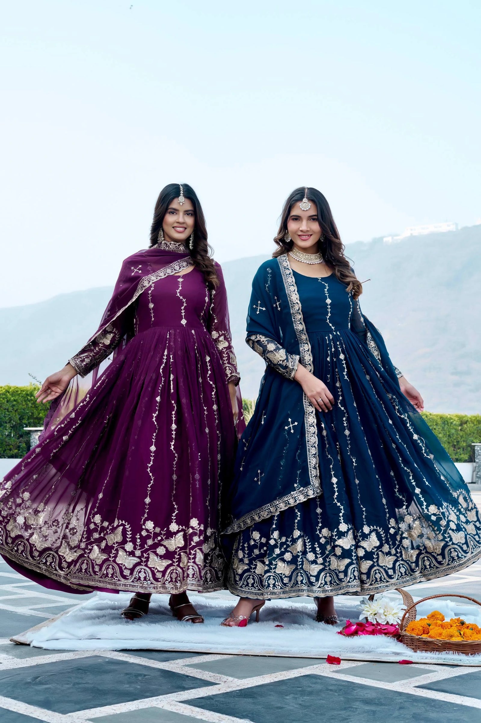 Two women in traditional embroidered dresses standing outdoors with a scenic background.