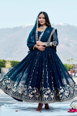 Woman in a traditional blue embroidered outfit with a scenic background