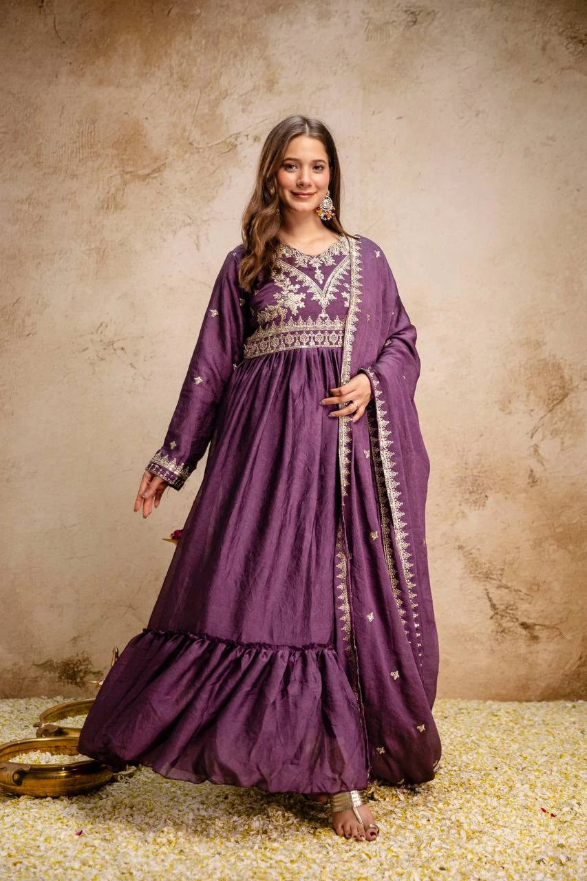Woman wearing a purple embroidered dress against a textured beige wall.