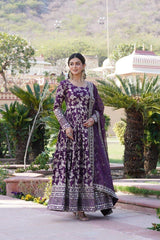 Woman in a purple traditional outfit standing in a garden with greenery and architectural elements in the background.