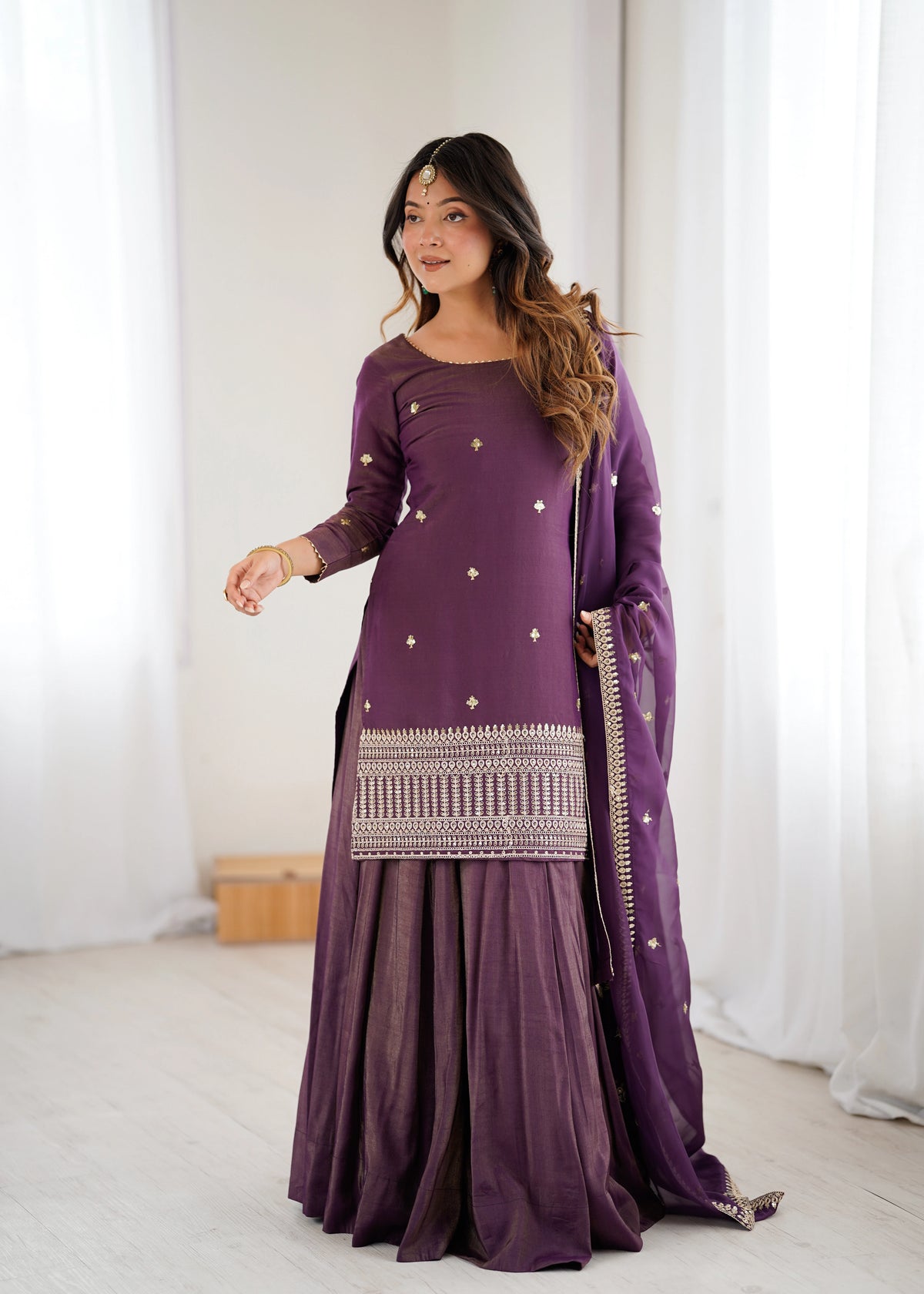 Woman wearing a purple traditional outfit with white patterns indoors.