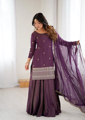 Woman wearing a purple traditional outfit with a matching dupatta in a minimal indoor setting.