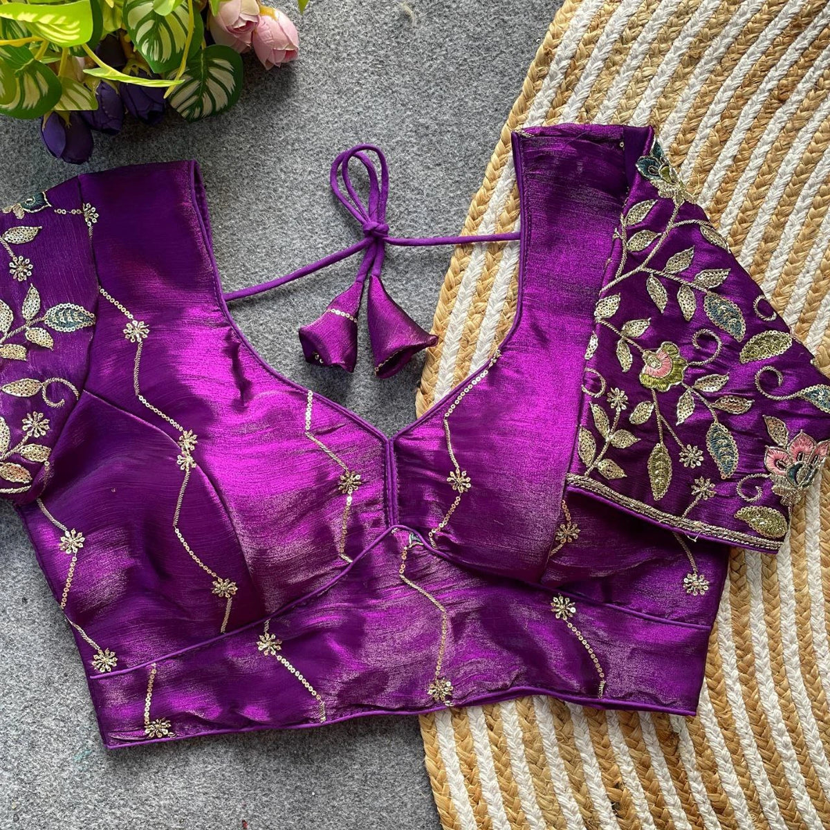 Purple embroidered blouse on a textured surface with flowers in the background