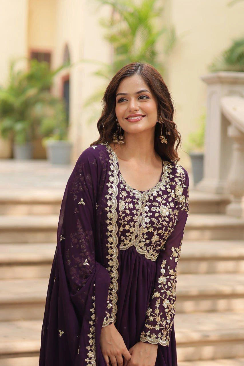 Woman in a purple traditional outfit with gold embroidery standing outdoors.
