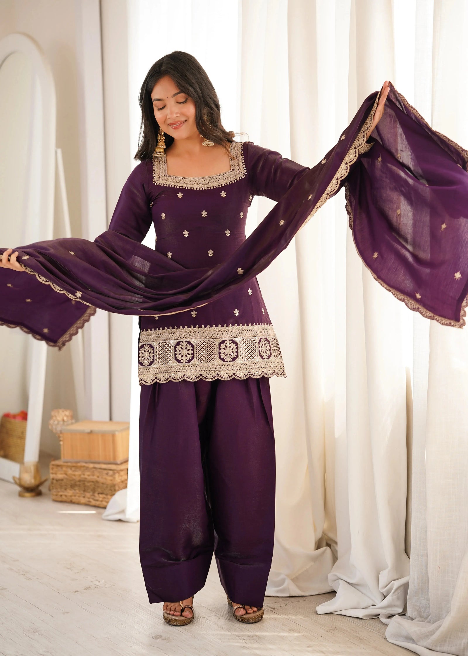 A woman stands elegantly in a deep plum traditional outfit with intricate silver embroidery.