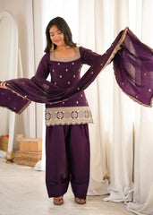 A woman stands elegantly in a deep plum traditional outfit with intricate silver embroidery.