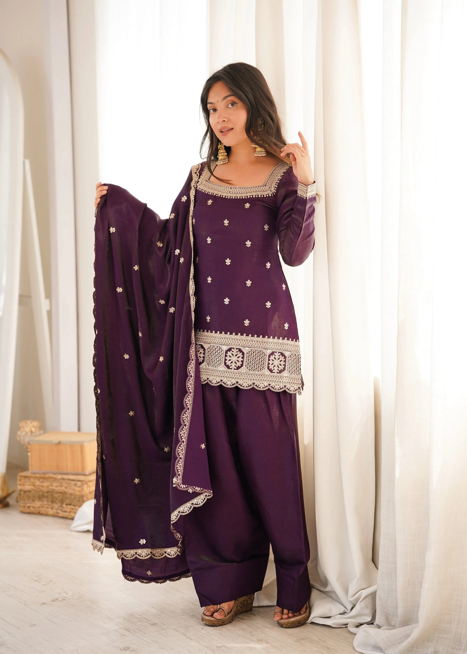 Woman wearing a purple traditional outfit with white patterns in a bright room.