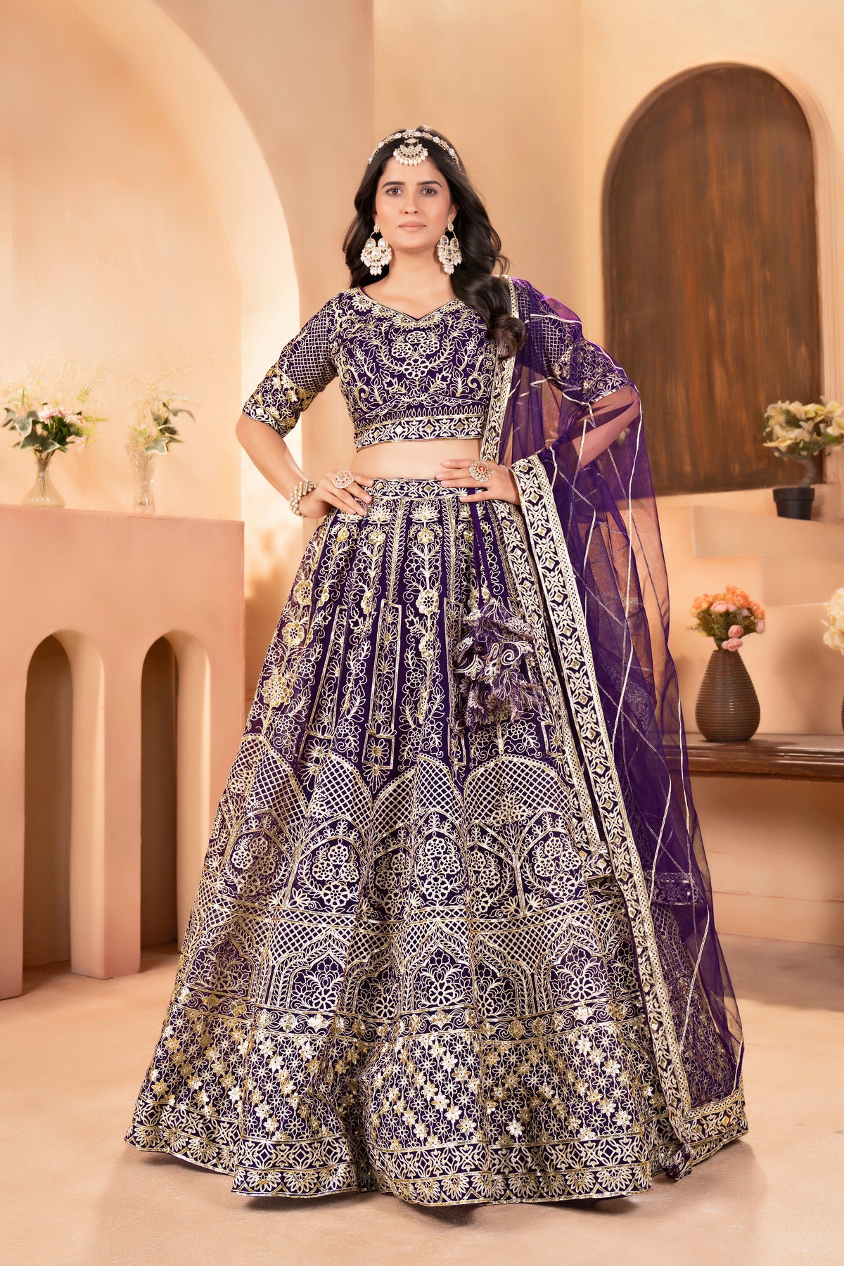 Woman in a traditional purple and silver embroidered outfit standing in an elegant indoor setting.