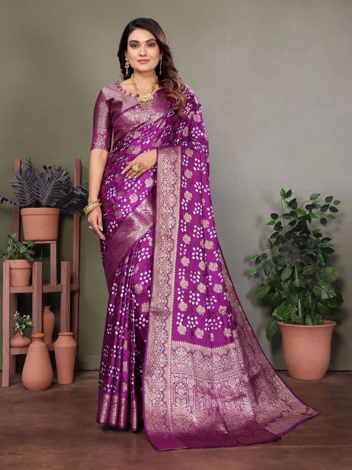 Woman wearing a purple saree with a pattern, standing against a neutral background with plants.
