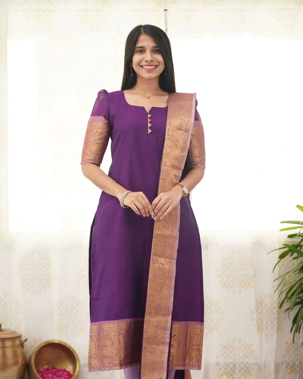 Woman wearing a purple kurta with a brown saree border against a light background