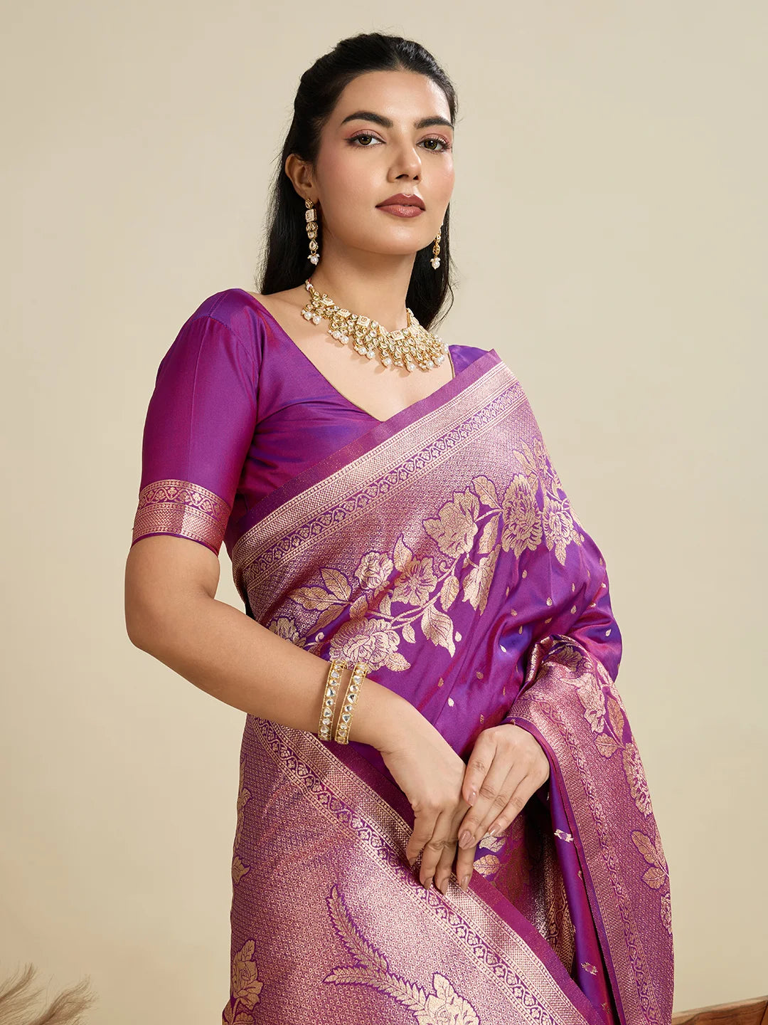 Woman wearing a purple saree with gold patterns on a beige background