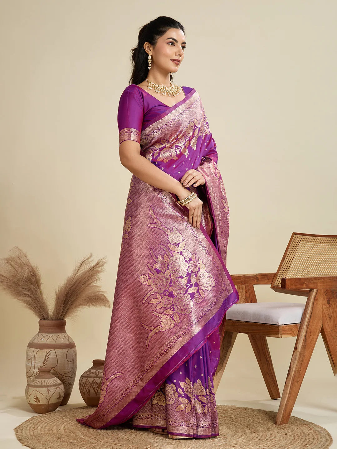 Woman wearing a purple saree with a floral pattern in a room setting.