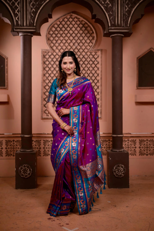 Woman in a purple and blue saree standing in an architectural setting
