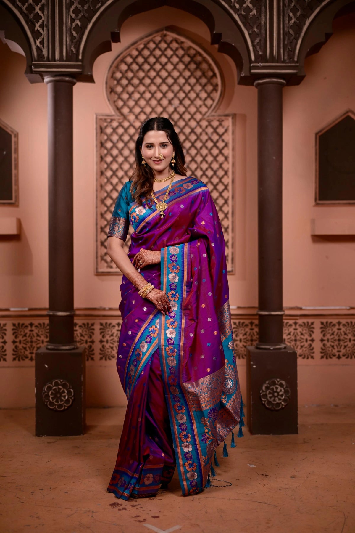 Woman in a purple and blue saree standing in an architectural setting