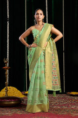 Woman in a green saree with a patterned border standing on a red carpet with decorative elements.