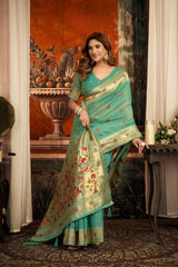 Woman in a green saree with floral patterns standing indoors.