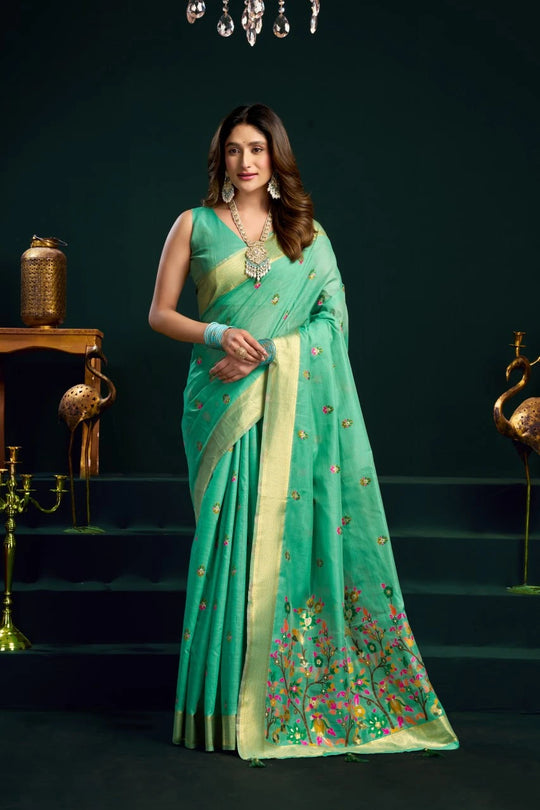 Woman wearing a green saree with floral patterns in an elegant indoor setting.