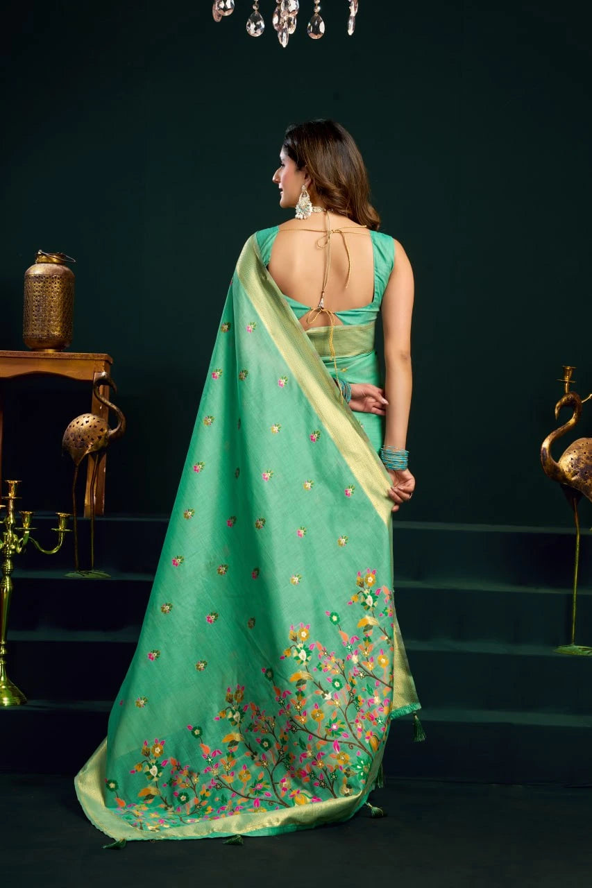 Woman in a green saree with floral patterns standing in a dark room.
