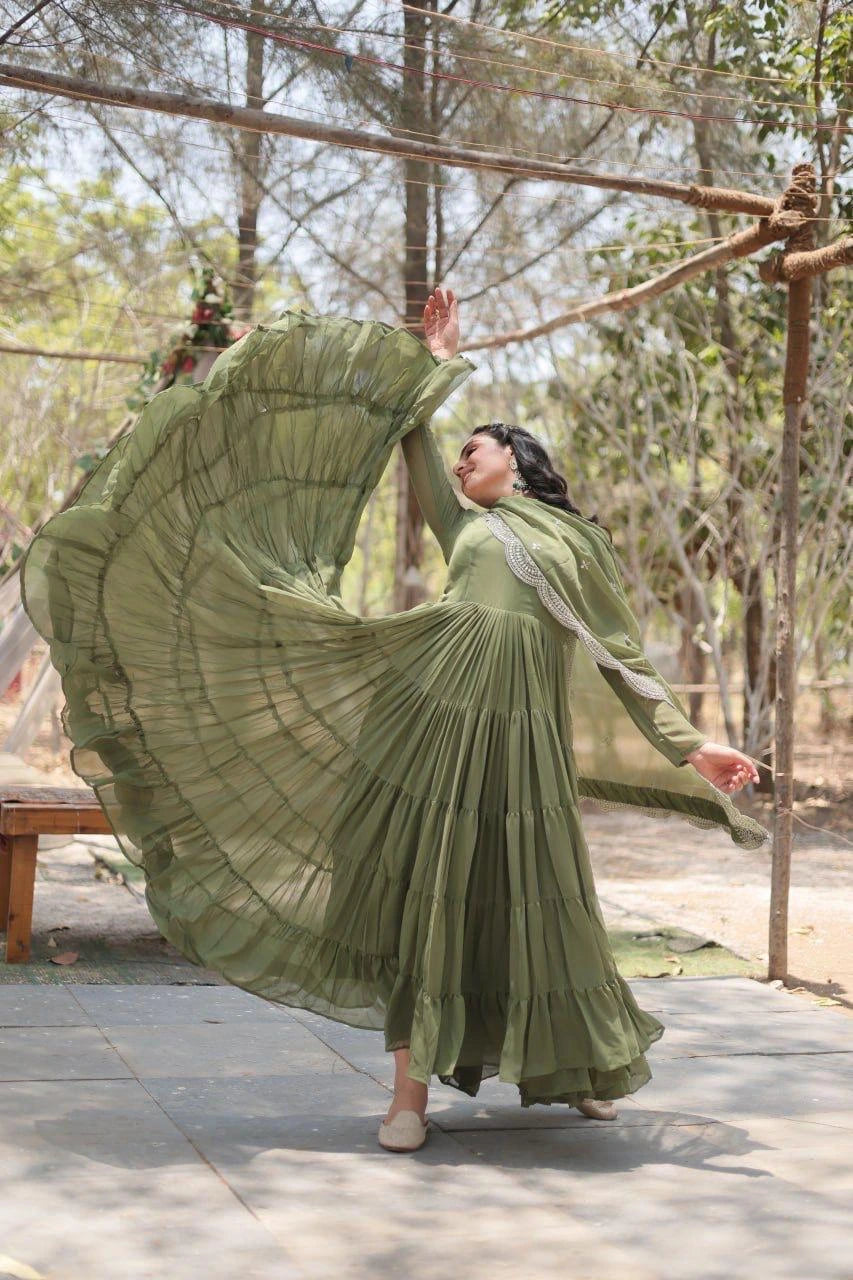 Woman in a long green dress with a wide skirt, standing outdoors with trees in the background.