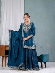 Woman in a blue traditional outfit with silver embroidery standing in a room.
