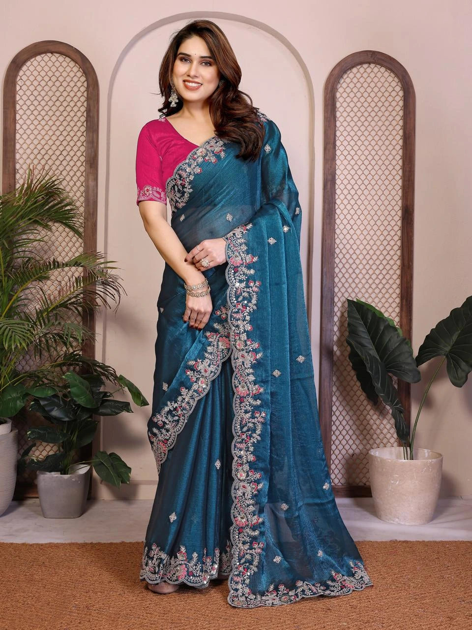 Woman wearing a blue saree with floral patterns in a decorated indoor setting.