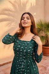 Woman wearing a green patterned dress standing outdoors with plants in the background