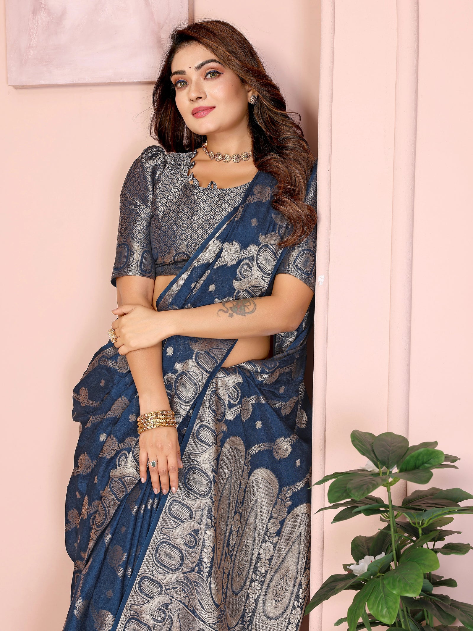 Woman wearing a blue saree with a white pattern against a light pink wall.