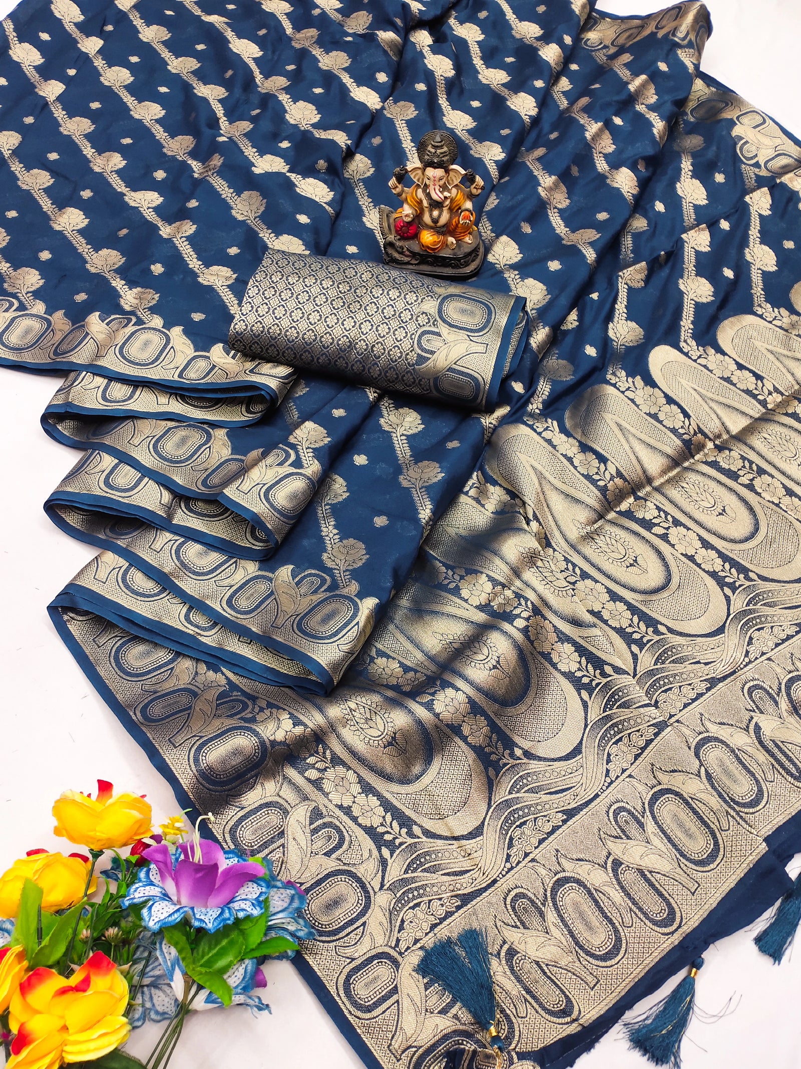 Blue and beige patterned saree with a small statue and flowers on a white background
