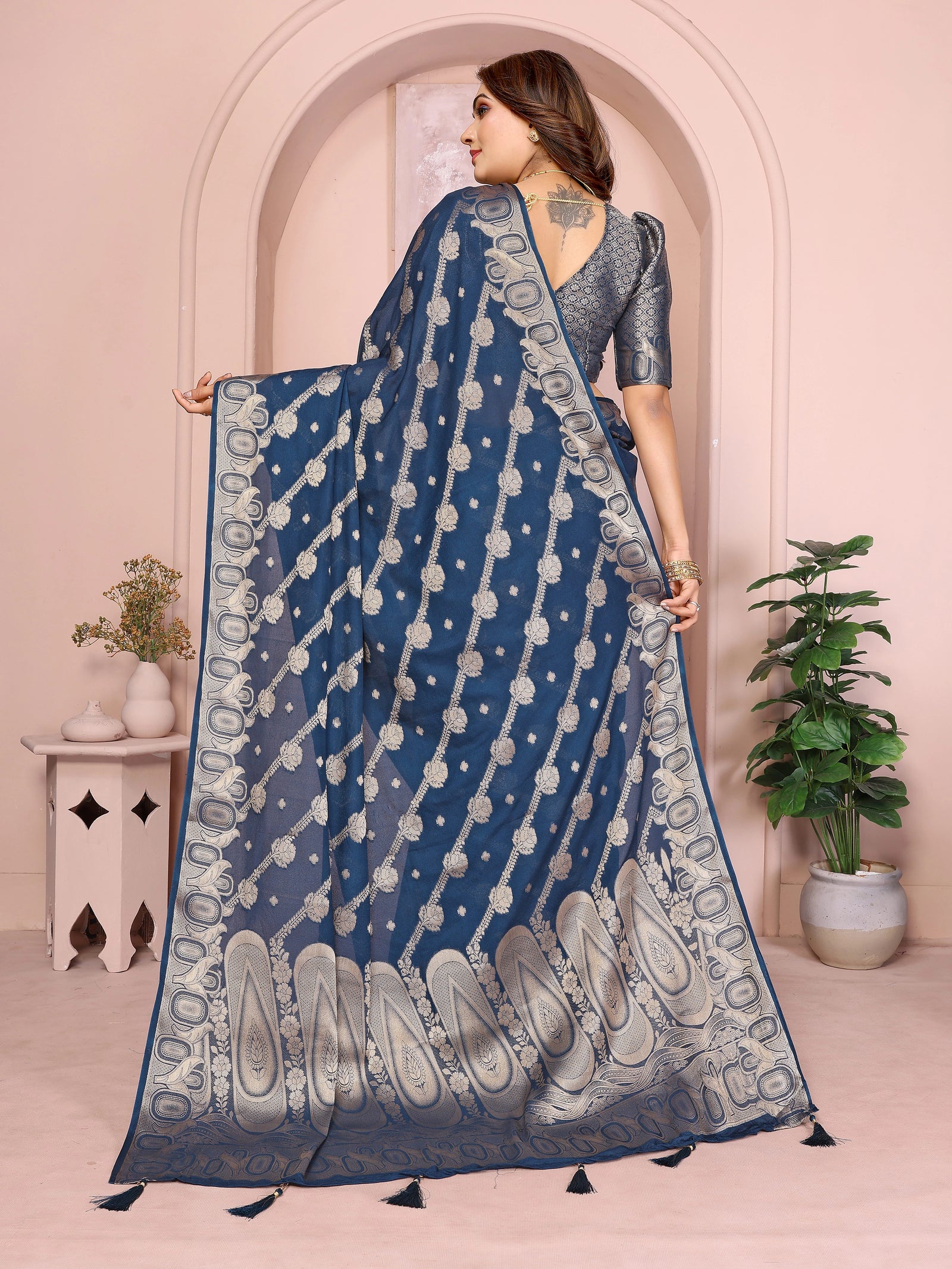 Woman wearing a blue saree with a white pattern in a decorated room.