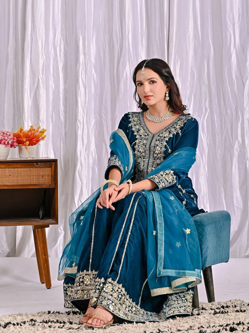 Woman in a blue traditional outfit sitting on a chair with a white curtain background