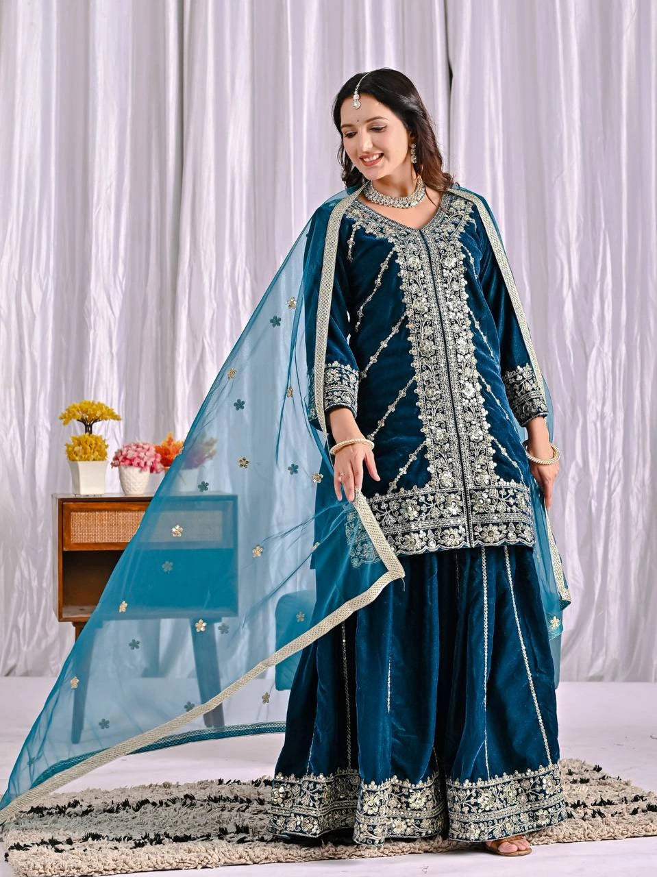 Woman in a traditional blue and silver outfit with a white curtain background
