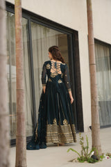 Woman in a dark green and gold traditional outfit standing in front of a modern building.